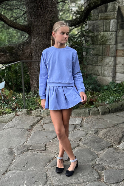 Person wearing a blue dress standing on a stone path with a stone wall and tree in the background