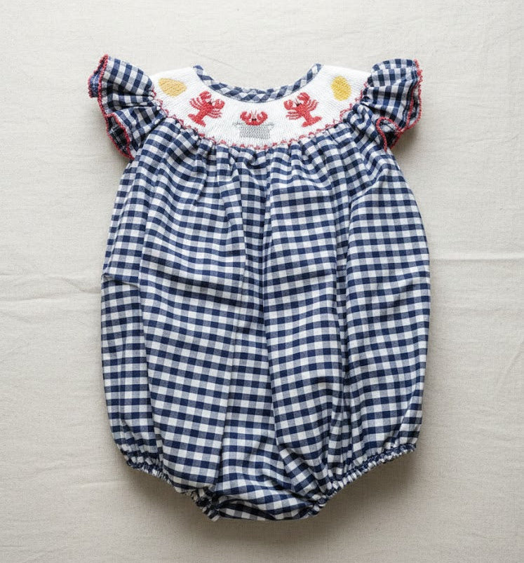Blue and white checkered baby romper with ruffled top on a light gray background
